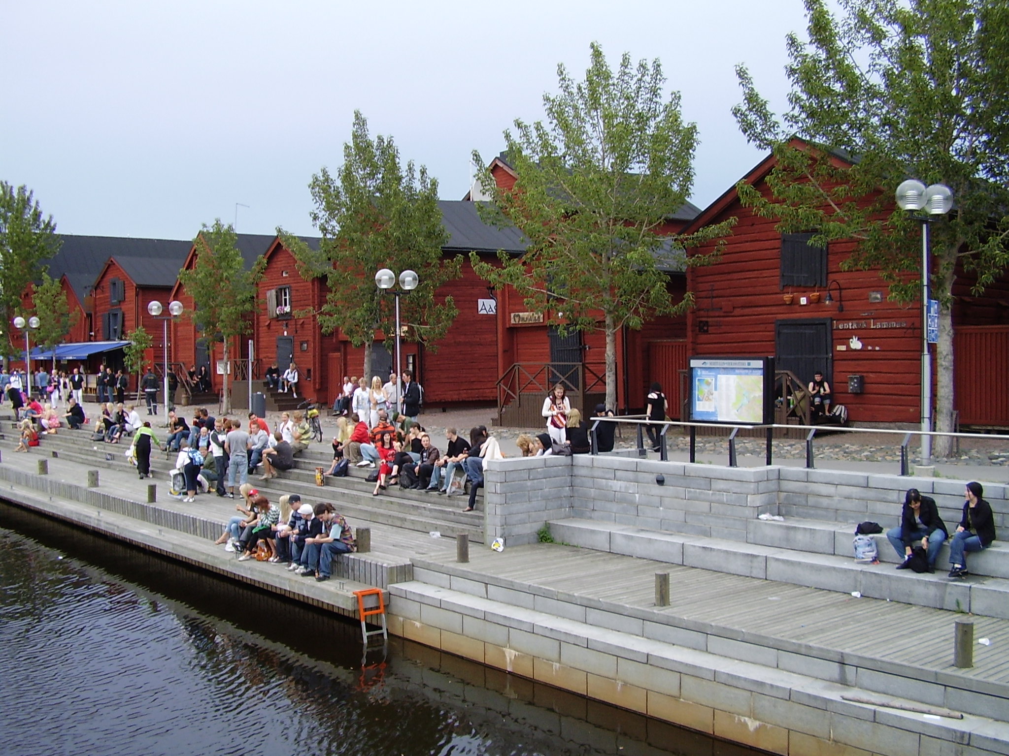 Personas junto al agua y los antiguos almacenes rojos del puerto de Oulu